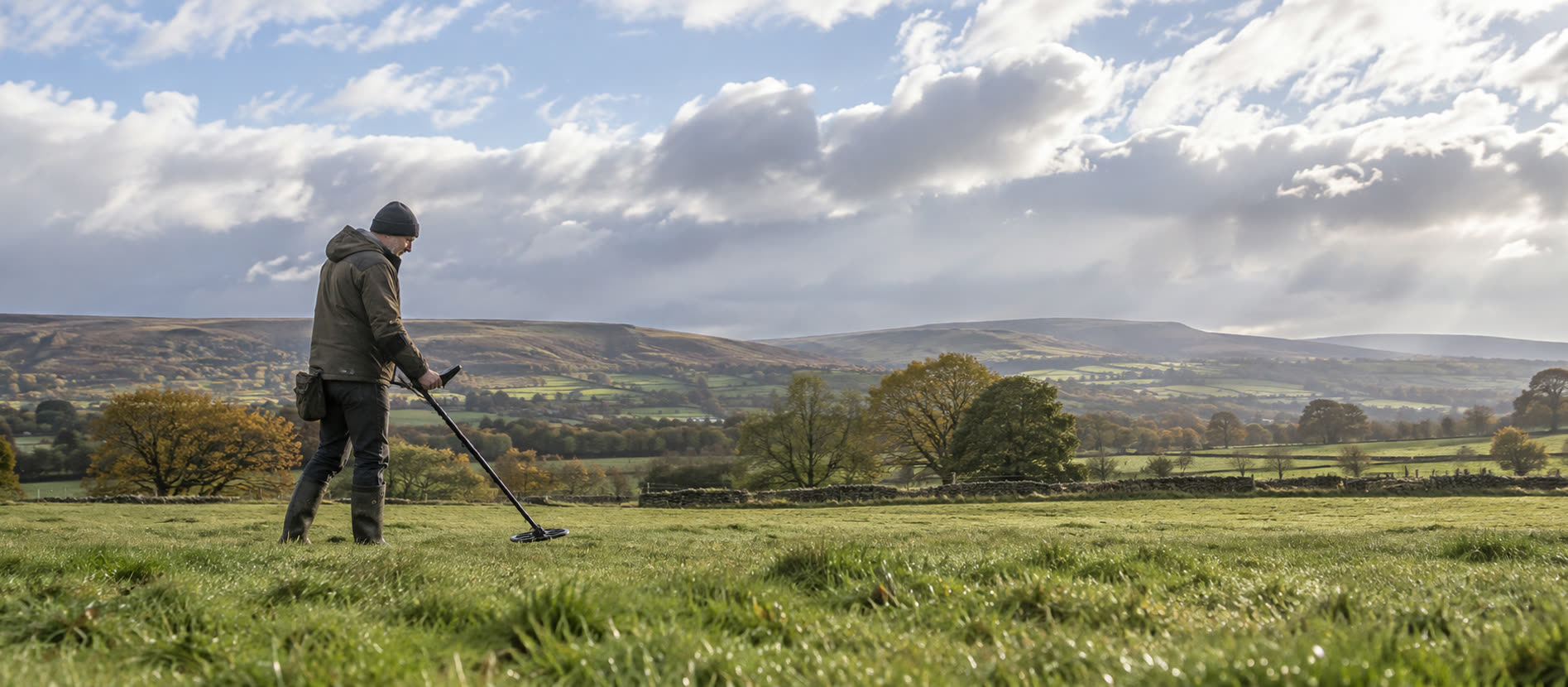 Detectorist sweeping firm damp pasture under clearing skies after rain