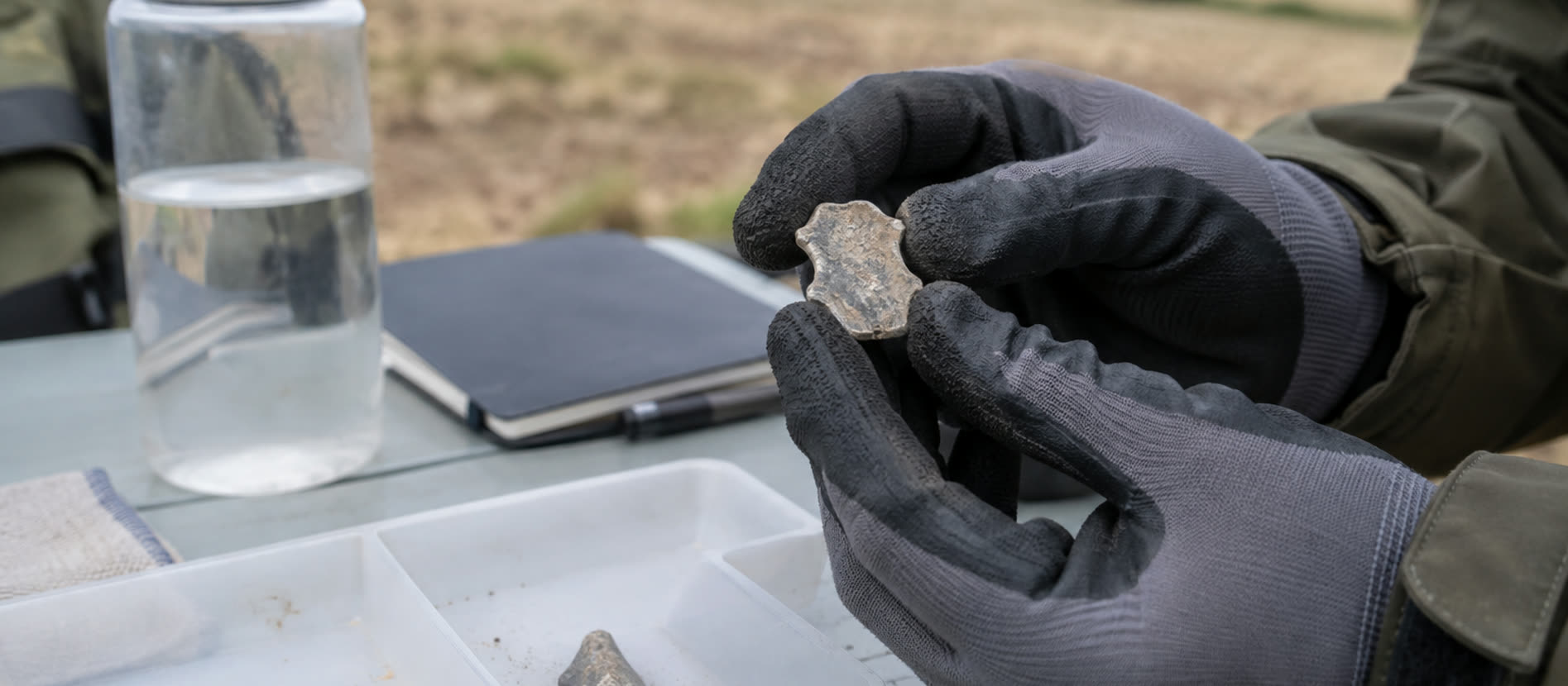 Gloved hands examining an ordinary dull grey metal fragment above a tray
