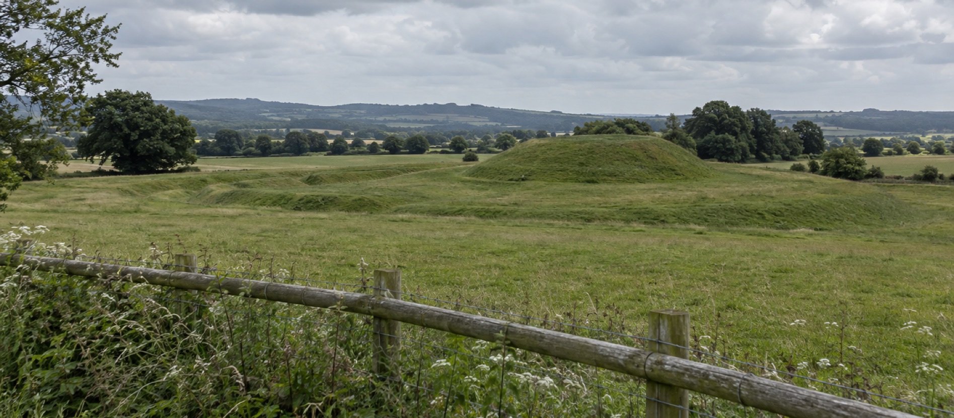 Ancient grassy earthwork seen beyond a protective fence