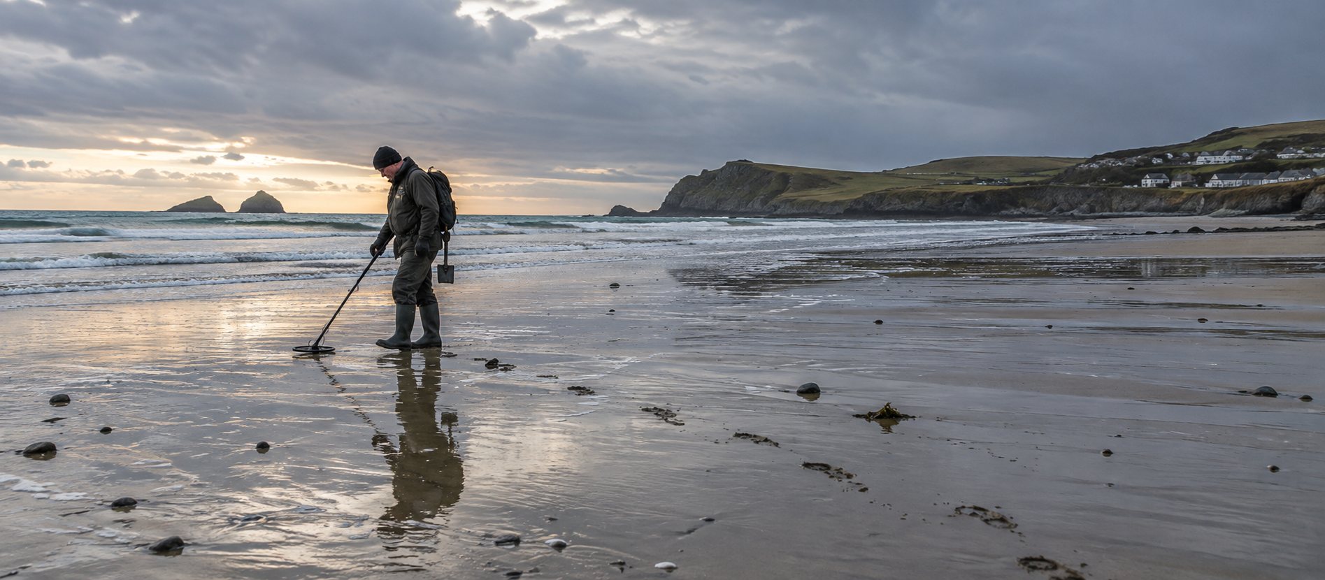 Detectorist searching reflective wet sand on a broad British beach